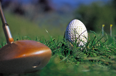 A white, dimpled, grass-stained ball is nestled on the turf